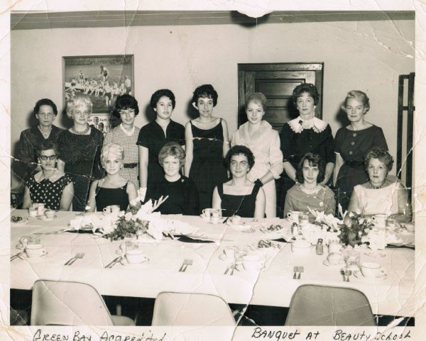 Group portrait of women at a banquet at the Green Bay Beauty School. In the back row, fourth from the left, is Frances Decorah. Handwritten at the bottom is: "Green Bay Accredited" and "Banquet at Beauty School." 