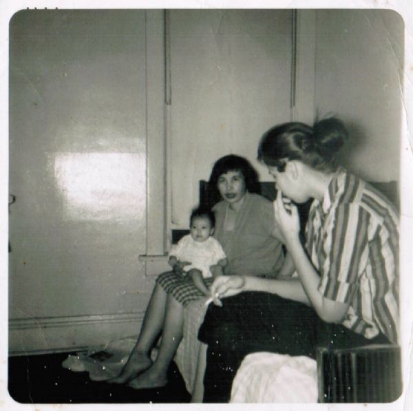 Two women are sitting on a sofa, with an infant on the lap of the woman in the background. 