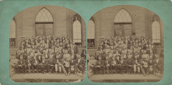 Stereograph of a group portrait taken on the front steps of a church. People are also visible in the open windows. The group consists of mostly men, one woman is looking out of the window on the left. A sign on the church reads, "Washington Av. S." On the reverse is written, "Synode Presterne."