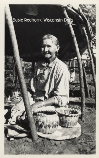 Susie Redhorn "HiNukIGa" (Woman), daughter of Frank Redhorn and Lucy Prettyman, shown in later years posing by two baskets. The photo was taken at the Dells Park Indian Village where she camped every summer.