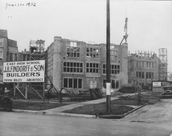Madison East High School construction site. The sign on the left reads: "East High School, J.H. Findorff & Son Builders, Frank Riley, Architect." The sign on the construction shack reads: "Electrical Work by Nickles."