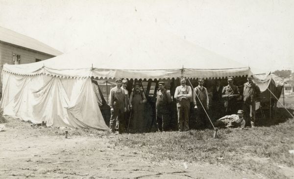 Group portrait of men posing in front of a tent set up outdoors as temporary headquarters for Findorff after a fire. Caption reads: "After the destruction of his plant by fire Mr. Findorff set up temporary headquarters for his men in a tent and borrowed the money to rebuild his business."