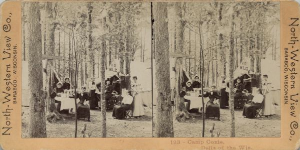 Stereograph of a group of women camping in the woods. They are wearing dresses, shirts and blouses, and hats. The women are sitting or standing in the clearing between two tents, among chairs, tables and a trunk. Utensils and other camp necessities are hanging on the trees. The tent on the right has the letters "HQ, M.L.G." above the opening. A tree on the left has a wooden sign nailed to it that reads: "Don't Hitch to the Trees." Caption on foot: "123 — Camp Coxie, Dells of the Wis."