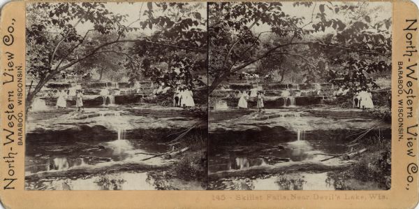 Stereograph of a group of women exploring Skillet Falls, some of them walking on the rocks. In the background is a horse-drawn buggy with a man and woman sitting in it. Caption at foot: "145 — Skillet Falls, Near Devil's Lake, Wis."