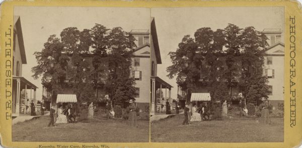 Stereograph of the Kenosha Water Cure on the corner of N. Main and Grand Avenue. Several men and women are strolling on the grounds, and two people are sitting in a glider with a shade. Built in the 1840s for educational and religious purposes, it burned down in 1900.<p>Text on the reverse: "Kenosha Water Cure, Kenosha Wis. Homeopathic and Hygienic Institute. N.A. Pennoyer, M.D. Physician. E. Pennoyer, Proprietor. This Institution, the oldest in the Northwest, has been under its present management for over 17 years. It has been the aim of the proprietor to make it in comfort, and in the facilities for the treatment of Chronic Diseases, equal to any establishment in the country. A building with large airy rooms has just been completed, which affords accommodations that the patronage of the "Cure" has for some time needed. Located but a few rods from, and overlooking the City, Harbor and Lake Michigan, with excellent grounds, convenient and safe boating, shaded walks and pleasant drives, it forms a most desirable resort for those needed rest or treatment. The summers at Kenosha are remarkably cool and pleasant, and particularly invigorating to those who suffer from the extreme heat of the interior. The Autumns and Winters are correspondingly mild and agreeable, the large body of water modifying the temperature of the air during those seasons.<br>Besides ordinary baths, its Electro-Termal, and Vapor baths are very efficient aids in the treatment of many diseases, Hadfield's Equalizer, the Health-Lift and compound Oxygen by inhaltion, have each served a valuable purpose in controlling morbid conditions of the body. During the last year, the Nuero-Dynamic system of medicine, as practiced only in Europe, has been introduced. In the treatment of Spinal irritations, nervous disorders, and functional diseases--particularly those of women, it has proved a most valuable adjunct.<br>The table of the "Cure" is liberal, it being believed necessary to sustain and build up the system by a plentiful and nutritious diet; each case, however, receives attention in this particular, and the proper quantity and kinds of food needed, are prescribed.<br>Dr. N.A. Pennoyer attends to the treatment of patients. His thorough knowledge of all the requirements of a hygienic institution, as well as his unusual opportunities for the study and treatment of chronic diseases, render him capable, with the many advantages at hand, of attaining more than ordinary success. Circulars, terms, etc., may be had on application.<br>Kenosha, Aug., 1875."</br></p>