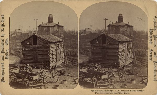 Stereograph of an old log structure surrounded by buildings, wagons and wagon parts, fences and trees. It was demolished about 1900. Text printed on the front: "Photographed and Published by L.H. Cook, Delton, Wis." "Curiosities Beauties and Attractions of Wisconsin Scenery." "Sparta and Vicinity, 'An Ancient Land-mark.' For Description, see other side."<p>Text printed on the reverse: "An Ancient Land-Mark--A Tribute.<br>The subject of this sketch whose portrait appears on the face side of this card, holds the same relation to the city of Sparta, that the acorn does to the tree. It was built by R.J. Castleman in the fall of 1851, and still occupies its former site on the borders of Beaver Creek. Its first covering was made of "oak shakes" stayed with poles; after being well chinked the "rough places were made smooth," within and without, with several coats of "mud plaster," after which it served as a residence for Mr. Castleman and family; it was also immediately converted to a hotel for the convenience and comfort of the weary traveler.<br>The winter following, the Rev. Frederick Walrath (now deceased) of the M.E. persuasion, caused its walls to echo with its first holy invocation, and spake to the few who assembled, the gracious words of LIFE. In the spring of '52 a postoffice was opened in one corner, the mail arriving regularly once a week from La Crosse.<br>In the fall following G.H. Ledyard rented the front room and filled it with goods, opening the first merchantile establishment within the "Ancient Landmark's" walls.<br>Here Dr. G.W. Millegan also made his home for several years during Sparta's early days.<br>Thus, it served as "residence," "hotel," "store," "postoffice," "medical dispensary" and a "place of worship;" and, although well advanced in years it has not yet wholly outlived its usefulness, being now used as a "storage building" by Andrew Thorbus.<br>Ah! Ancient landmark! while in deep meditation we stand gazing upon thy quaint old weather-beaten and time-worn sides, thou seemest to tell of joyous and sorrowful scenes, of hardships endured and victories gained, of pleasant greetings and painful partings, of happy marriages and sad deaths which have transpired within thy rustic walls in the days and years gone bye. What a history thou could'st give us, what a tale thou could'st unfold, what incidents thou could'st disclose if thou had'st but the power of speech! but as thou art fast crumbling by decay, and soon will be numbered among the things of the past, therefore, as a tribute to thy sacred memory, we photograph thy wasting form, from which we will prepare mementos and offer them to the residents of this beautiful city now surrounding thee, of which thou wert the forerunner, that in the years to follow they may have something with which to refresh <i>their</i> memory in reference to the first building erected on the site where now stands the fast-growing and prosperous city of Sparta with its 5000 inhabitants. The Publisher."</p>
