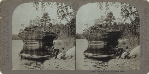 Stereograph of a formation on the Wisconsin River called "The Ink Stand." On the shore a woman is sitting on a wooden bench, and behind her is a picnic basket. A man is pulling his boat, "The Water Witch," onto the beach. On the far beach, beyond the Ink Stand, another man can be seen sitting. The caption reads: "5525 The Ink Stand, Wisconsin Dells. Copyright 1901 by C.H. Graves."
