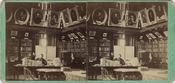 Stereograph of librarian Daniel S. Durrie seated in the two-story high gallery that the Historical Society occupied in the old South Wing of the Wisconsin State Capitol from 1866 until 1883. In addition to this room, the Society also filled the entire second floor of the South Wing — the same floor with the Senate and the Assembly. Dating to approximately 1880, this photograph is one of a very few that document the early appearance of the Third Capitol. Of note are the patterned carpet, table, decorative crown moldings, the gas chandelier, and the library cabinets. Carpets are known to have been changed in the Capitol, and it is unlikely that the patterned design here is original. The photograph also documents the prominent role of the Society's painting and art collection. Framed portraits are lined up along the ceiling and the tops of the bookcases. Hand-written on the reverse, "State Wis. Rooms, Madison, Books."

