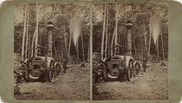 Stereograph of a portable steam powered engine, outdoors in the woods. The wheels are set on thick planks. The engine is being used to power more machinery in the background where steam is escaping from a pipe. The door to the firebox is open. A workman is sitting on a barrel against a front wheel. Other men are posing between the engine and the machine. Text just above the firebox reads: "Ames Iron Works, Oswego, N.Y., below, No. 3." Text on the reverse: "Stereoscopic Views, -of- Florence and Commonwealth. Harvey's Exploring Eng. -Published By- Wm. Collins. Neenah, - - Wisconsin."