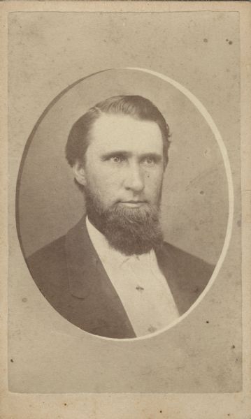 Carte-de-visite, quarter-length, quarter-length studio portrait of a man, framed by an oval matte. He is wearing a suit and has a full beard. On the reverse is printed: "Miss T.B. McCafferty, Photographer, Over Fuller Bros. Store, Columbus, Wis." 