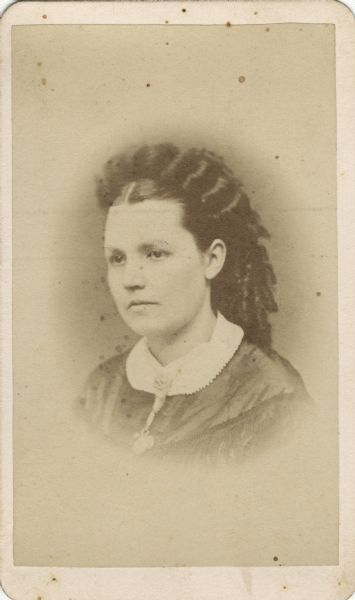 Carte-de-visite, quarter-length portrait of a woman inside an oval vignette. She is wearing a dress and has curled hair. On the reverse is printed: "Miss T.B. McCafferty, J.A. Ridgway, Operator, Columbus, Wis." 