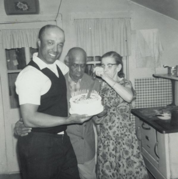 Lewis Arms standing with his uncle Bernard Arms, and aunt Nellie Arms. Lewis is holding a cake which was baked for Bernard's birthday.