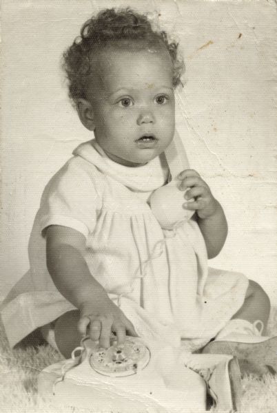 A studio portrait of Nancy Arms as a baby playing with a telephone.