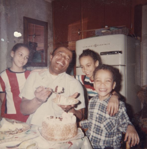 Lewis Arms is holding a slice of his birthday cake, and is surrounded by three of his children. From left to right are Rita, Lewis, Mamie, and Paul.