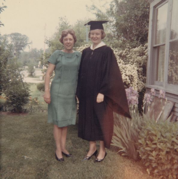 Janet Sauk standing outdoors with another woman (possibly her mother) on the day she graduated from the University of Wisconsin-Madison. She is wearing her cap and gown.