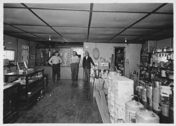 Three men are posing inside the Franklin Hardware Company and Eland Post Office. Jerome Francis Franklin Sr. is on the right, and two possible Franklin relatives are on the left. Merchandise fills the display cases on the left, and larger items are on the floor and shelves on the right. Behind the men on the back wall are the post boxes. Jerome Francis Franklin Sr. and his son Jerome Francis Franklin Jr. alternated in the job of Postmaster.