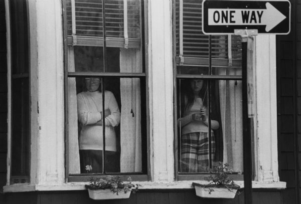 A woman and a teenage girl are looking out the windows of a building during unrest following court-ordered school desegregation busing.