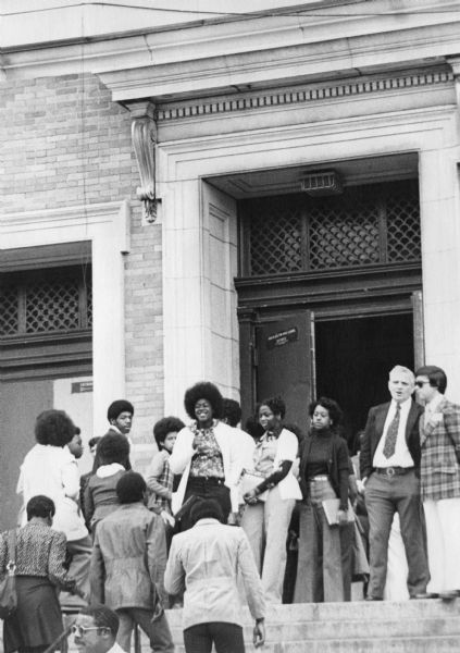 Students and three adults on standing on the steps at an entrance to South Boston High School. 