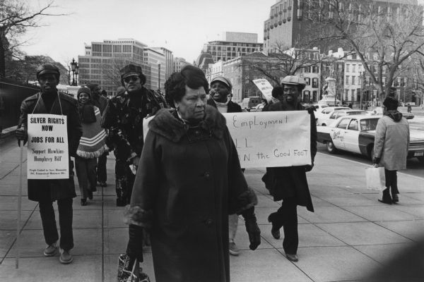 Demonstrators at a PUSH (People United to Serve Humanity) March walking around the White House to commemorate the 46th anniversary of the birth of Martin Luther King Jr. The march also supported the proposed Humphrey-Hawkins Full Employment Bill. An estimated 2000 people participated, carrying signs. One man has a sign that reads: "Silver Rights Now, Jobs for All, Support Hawkins-Humphrey Bill."