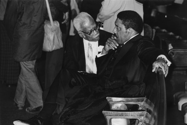 Two unidentified men, officers of PUSH (People United to Serve Humanity), sitting and talking together at an event.