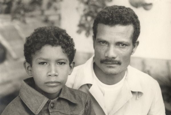 Casual outdoor portrait of a man and a boy. Caption on the reverse reads: "Ramón and the first black president of Ecuador, Moncho (and the first honest one too)."