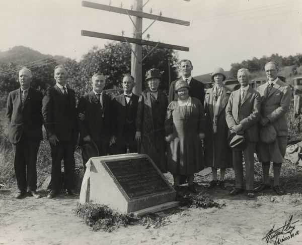 Group portrait of attendees at a ceremony to place a marker on the former site of the French post of Nicolas Perrot. From left to right are Dr. Eben D. Pierce, Judge Hans A. Anderson, Professor John Holtzinger, John A. Latsch, Louise Phelps Kellogg, Mrs. Louis Hill, Judge E.F. Hensel (behind Mrs. Hill), Edna L. Jacobson, Professor Albert H. Sanford, and Louis Hill.
