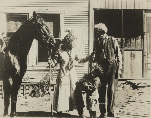 Actress Josie Sedgwick plays Betty Clayton in this western. Betty is in charge of the Lazy Y ranch, and her young brother Bobby lives with her. Her grandfather wanted a safe home for his grandchildren. This exterior image shows Betty holding her horse's reins in one hand and a rifle in the other while she speaks with an older man, probably her grandfather, while Bobby looks on. Scene may be at the Lazy Y ranch.

