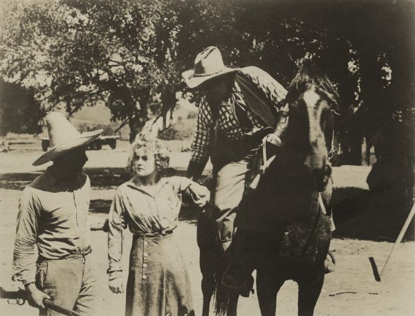 Actress Josie Sedgwick as Betty Clayton runs the Lazy Y ranch for Calumet Marston, who is in a feud with Neal Taggart and his father Tom. Betty is with two men, both of whom hold onto her arms. One man is on a horse. Betty is looking with defiance or anger at the second man, who is holding a rifle.