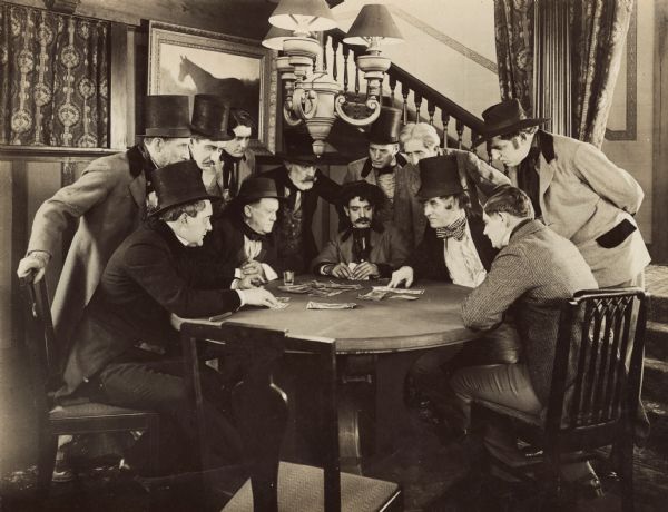 Film still of group of well-dressed men at a table playing a game of cards; money is on the table.