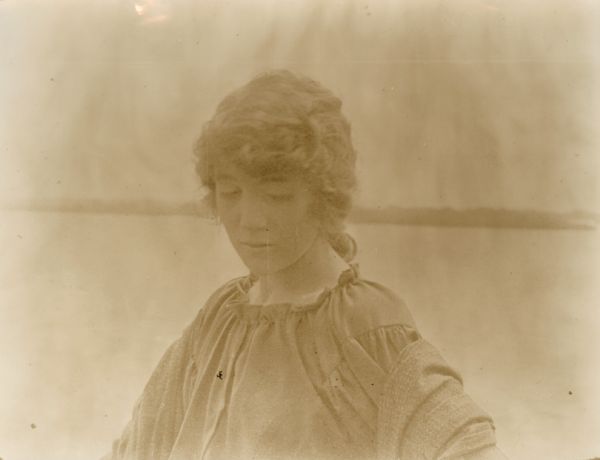 Film still of an exterior with a woman; river in the background.

 	