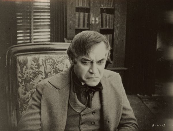 Film still of interior, a well-dressed man sitting, glum expression.