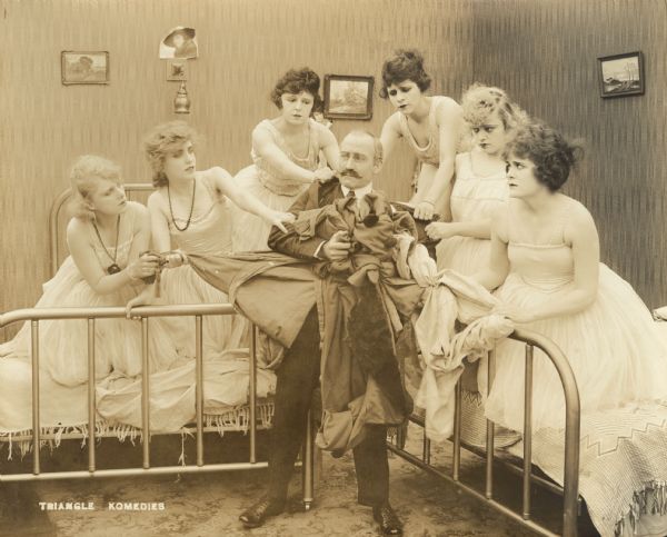 Film still with one actor and six actresses in an interior setting that may be a dormitory.
