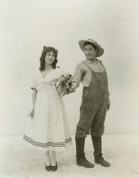 Film still depicting a young man handing a bouquet of flowers to a young woman; no scenery.

