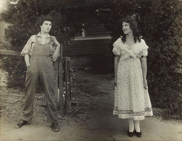 Film still - exterior - depicting a young man and young woman looking at each other. The man is played by the actress playing the young woman shown in the scene.     
	
