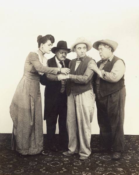 Film still - interior - group of one actress and three actor standing together; no set beyond carpet on the floor.