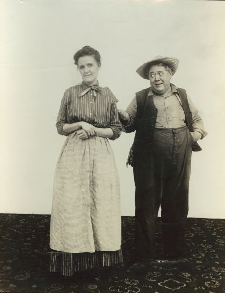 Film still - interior - actress and actor standing together; no set beyond carpet on the floor.	
	