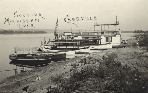 Postcard labeled in photographer's hand: "Souvinr [sic] Mississippi River, Cassville." A Frank Feiker 'Souvenir' postcard of several excusion boats on the beach with American flags in the stern.