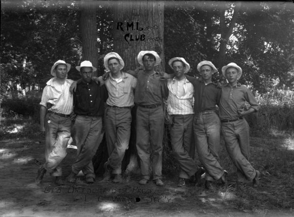 A group of seven men posing in front of a tree with their arms over each others shoulders. George Ortscheidt, President; L.G. Ward, Secretary.
