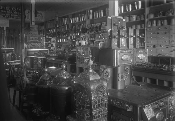 View of the interior of Tate & Kleinpell Hardware, with stoves, churns, seeds and other items displayed for sale.