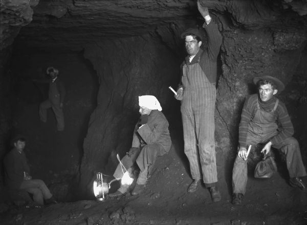 Interior of a lead mine. The five miners are holding candles or lanterns.