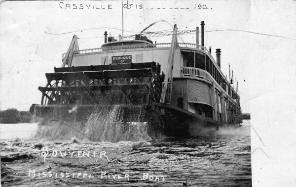 Rear view of the sternwheel paddle boat 'Dubuque of ?" on the Mississippi River near Cassville, Wisconsin. This postcard is marked 'Souvenir' by Frank Feiker, the photographer. Caption reads at top: "Cassville, Wis. _______ 190_." At bottom the caption reads: "Souvenir, Mississippi River Boat."
