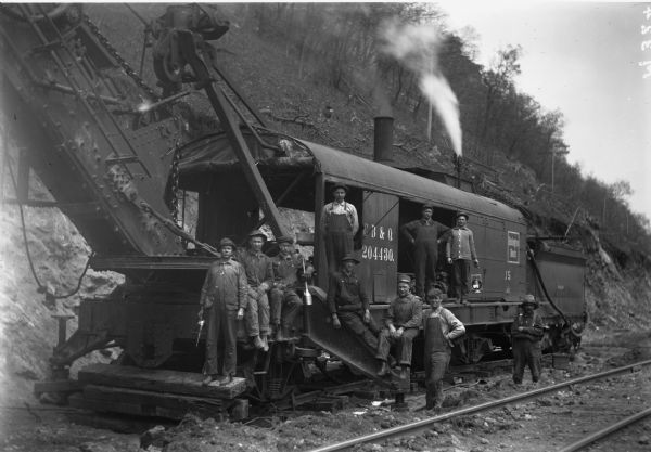 The Chicago, Burlington and Quincy Railroad crew with the rock crusher. The train car is labeled '204430' and 'Burlington Route'. A steep hill rises behind them.