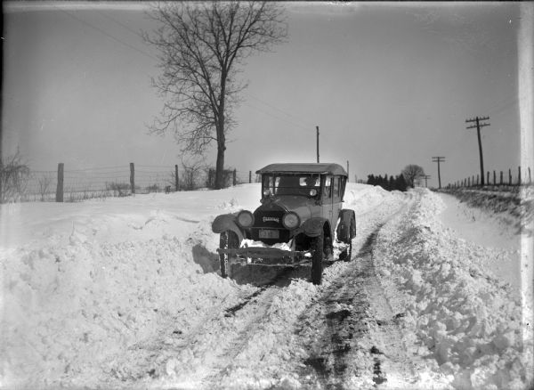 Winter scene with a man in an automobile on a snowy road.