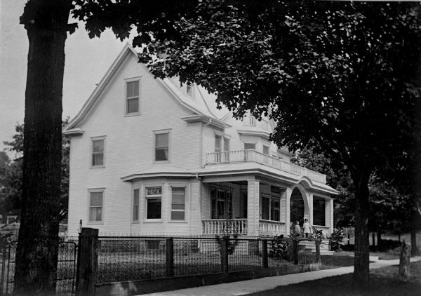 View from street of front and side of the Gus Klindt home. The house was owned by Noah Brinkman in 1951-1952. The yard is fenced and there are two children standing on the porch.