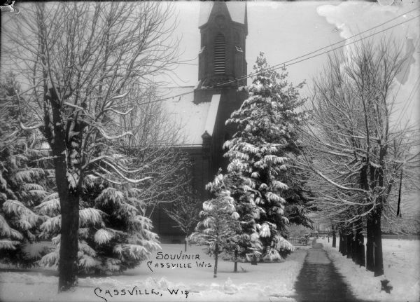 Winter scene with a church, Cassville, Wisconsin.  The evergreens and yard are snow-covered. The sidewalk has been shoveled.