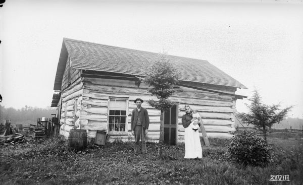 Ephraim Watt, his wife Rhoda Adelaide Watt (née Mosher), and their daughter, Glendora Eunice Watt, pose in front of their log home, 14 miles southwest of Florence. The image caption reads, "where we had dinner, Aug 2, 1895."