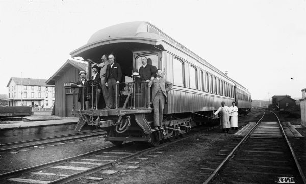 Group of surveyors from the Agricultural Department at the University of Wisconsin posing on the back platform of their railroad car 404, "the Palace Car." The men are: McKerrow, Riley, Thayer, Henry, Cleveland, and Pierce. Two other people pose along the tracks on the side of the car. In the background on the left is the Florence railroad station.