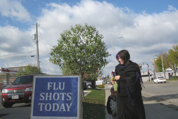 A mother is taking her child to the Cass Street Pharmacy, which is advertising flu shots.