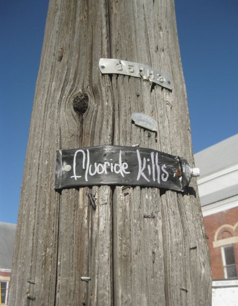 A toothpaste bottle painted with the words "fluoride kills" posted on a utility pole.