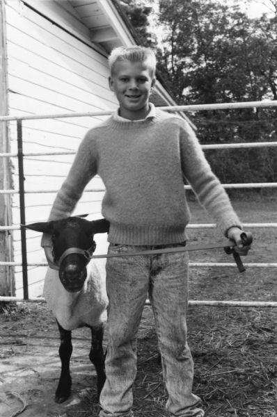 A male teen is posing with a prize sheep at the Adams County Fair.